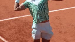 Carlos Alcaraz durante partida de tênis em quadra de saibro, com raquete em movimento de saque (imagem de arquivo, Roland Garros)
