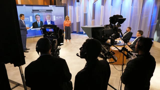 Estúdio de TV com equipe de produção acompanhando telão de resultados eleitorais