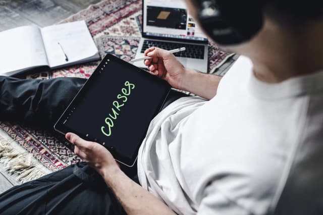 Pessoa sentada em casa usa tablet e notebook para estudar, remetendo à qualificação profissional oferecida pelos cursos gratuitos do Programa Trampolim na Baixada Santista