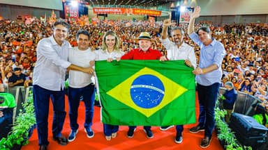 Imagem de arquivo: o presidente Lula, de camisa vermelha e chapéu de palha, segura uma bandeira do Brasil ao lado de aliados no palco da convenção da Federação Brasil da Esperança no Ceará, em 31 de julho, diante de um ginásio lotado