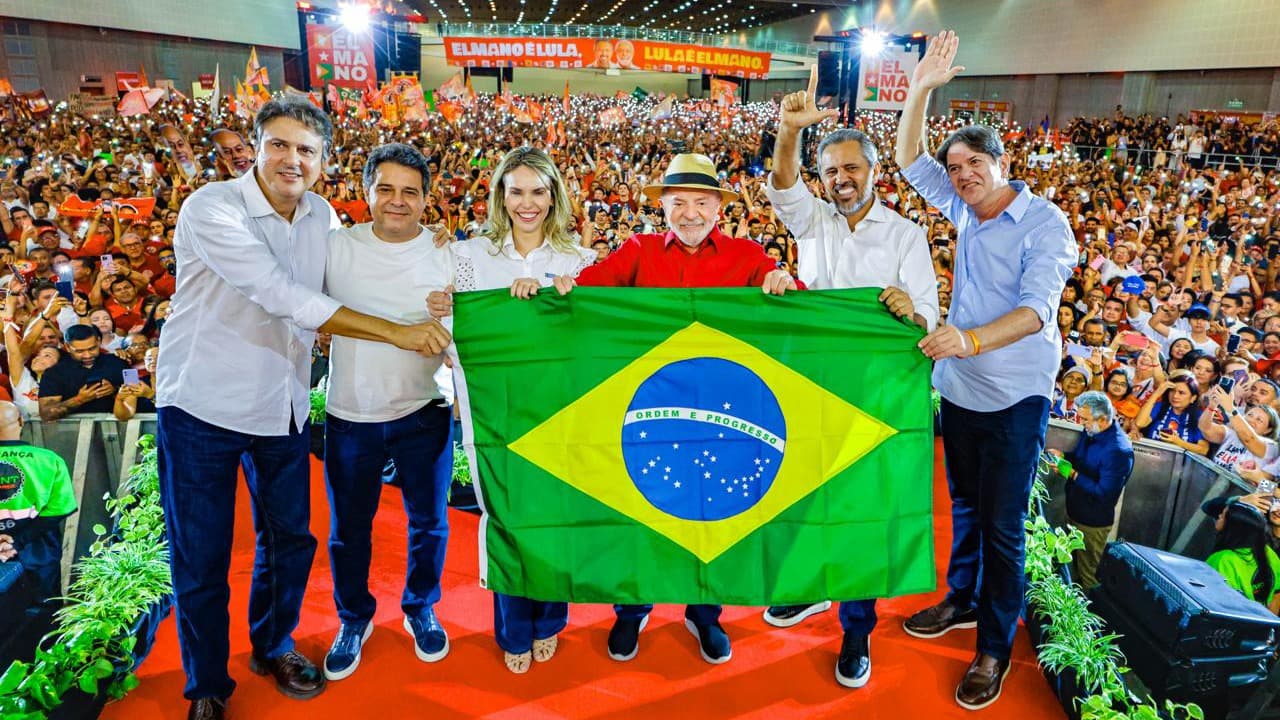 Imagem de arquivo: o presidente Lula, de camisa vermelha e chapéu de palha, segura uma bandeira do Brasil ao lado de aliados no palco da convenção da Federação Brasil da Esperança no Ceará, em 31 de julho, diante de um ginásio lotado