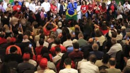 O presidente Luiz Inácio Lula da Silva discursa ao microfone, segurando uma bandeira do Brasil, diante de apoiadores
