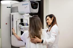 Profissional de saúde do Hospital Orizonti auxilia paciente durante exame de mamografia digital