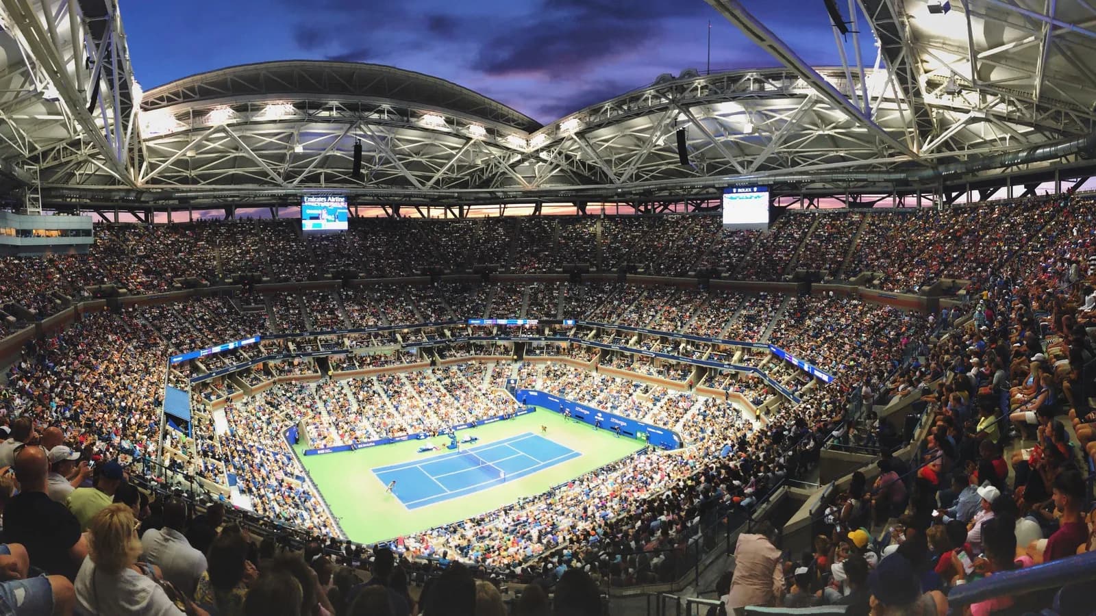 Arquibancadas lotadas da Arena Arthur Ashe durante partida noturna do US Open, com o público em volta da quadra