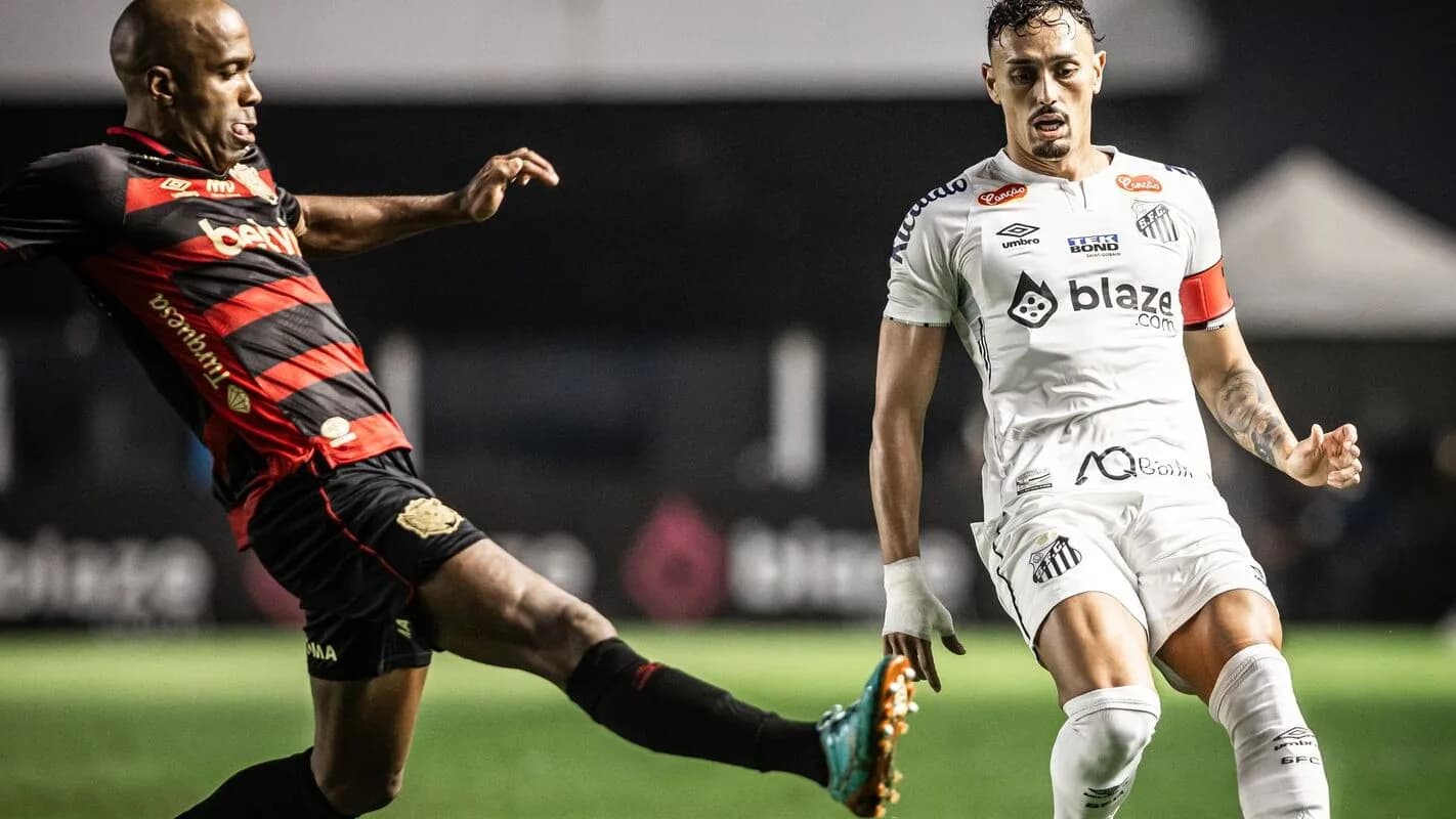 Jogador do Sport, de uniforme vermelho e preto, chuta a bola durante partida contra o Santos