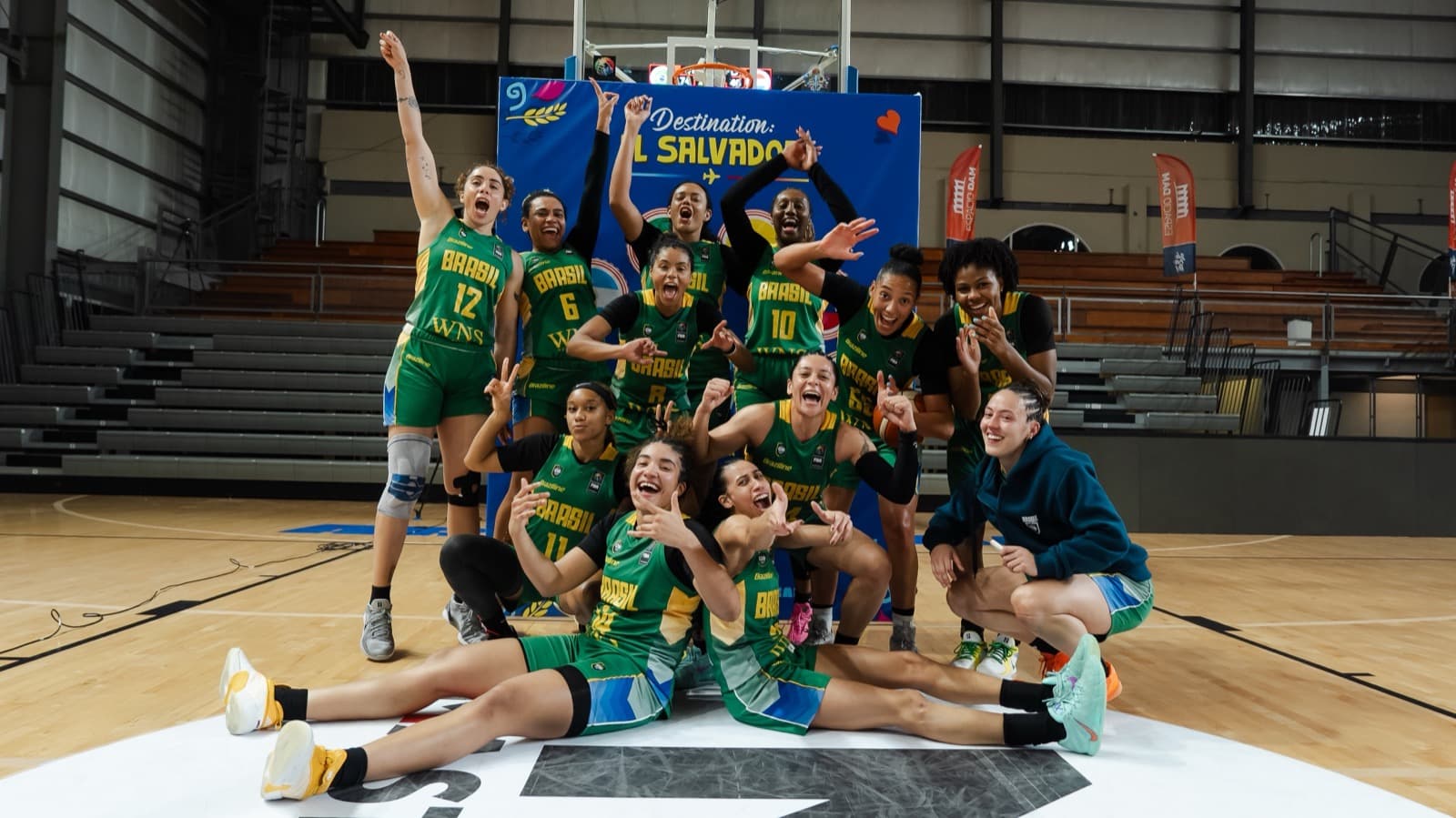 Jogadoras da seleção brasileira feminina de basquete comemoram classificação para a AmeriCupW 2027, com banner "Destination: El Salvador" ao fundo