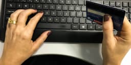 Mãos de uma pessoa usando cartão de crédito para fazer compra online no teclado do computador