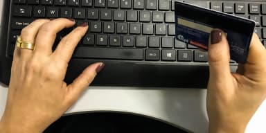 Mãos de uma pessoa usando cartão de crédito para fazer compra online no teclado do computador