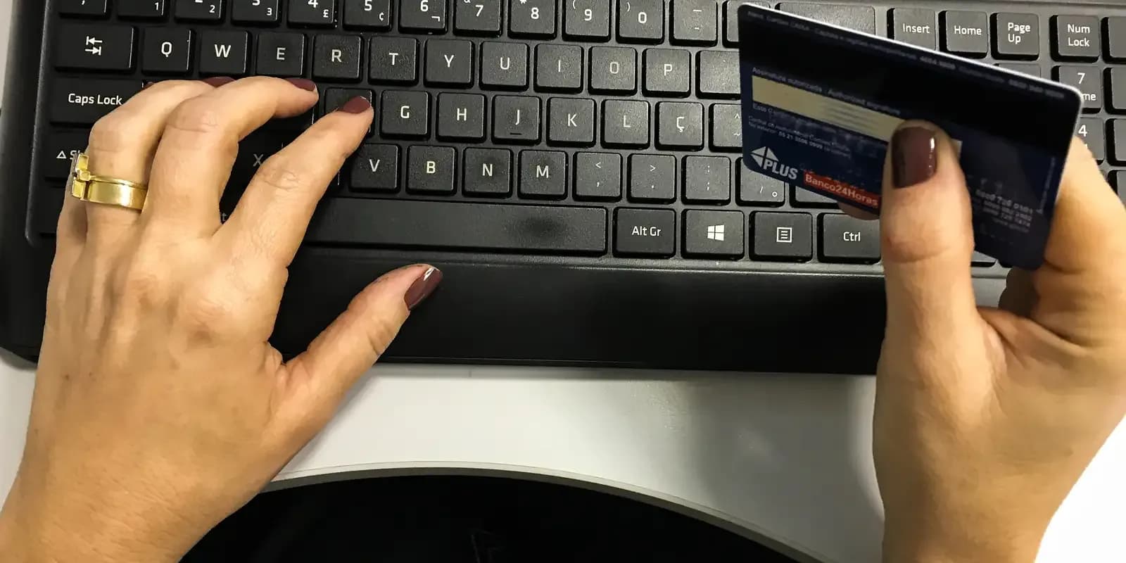 Mãos de uma pessoa usando cartão de crédito para fazer compra online no teclado do computador
