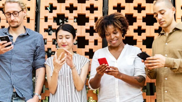Grupo de quatro pessoas usando celulares lado a lado