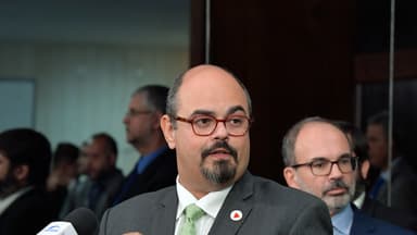 Mateus Simões fala a jornalistas em entrevista coletiva, de terno e com um pin da bandeira de Minas Gerais na lapela; imagem de arquivo de 2024