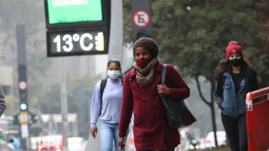 Pedestres agasalhados caminham por avenida de São Paulo em dia frio, com termômetro de rua ao fundo marcando 13°C