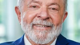 Retrato oficial do presidente Lula sorrindo, de terno azul e gravata com as cores da bandeira do Brasil