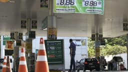 Cliente abastece veículo em posto de combustível, com painel de preços ao fundo (foto de arquivo)