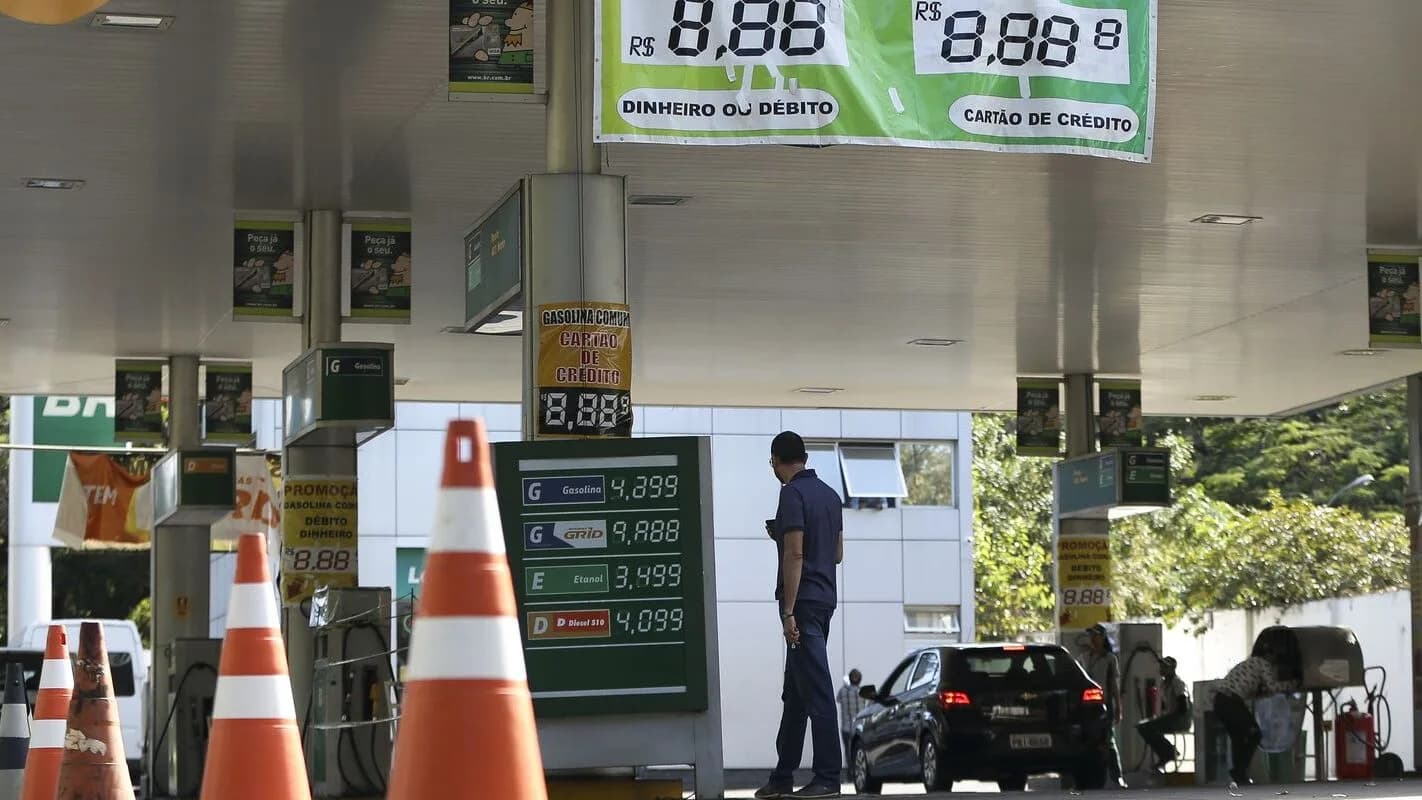 Cliente abastece veículo em posto de combustível, com painel de preços ao fundo (foto de arquivo)