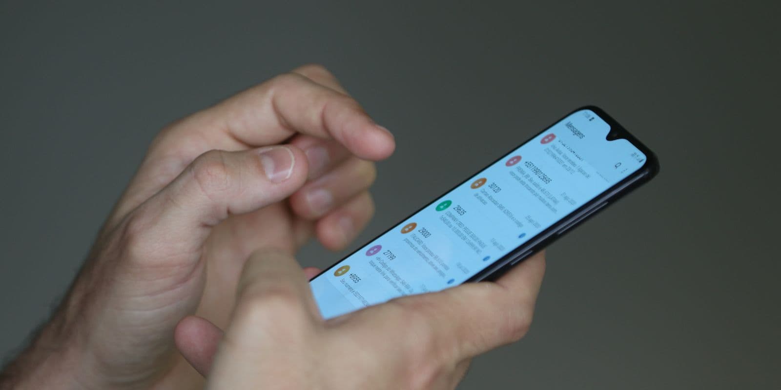 Mãos segurando um smartphone com lista de mensagens na tela