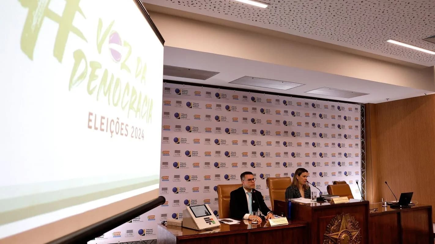 Mesa de autoridades em evento sobre participação eleitoral, com painel 'Voz da Democracia' ao fundo