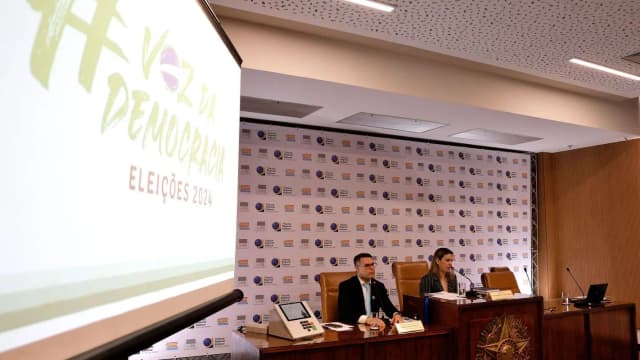 Mesa de autoridades em evento sobre participação eleitoral, com painel 'Voz da Democracia' ao fundo