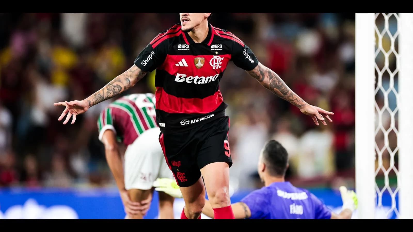 Jogador do Flamengo comemora gol com os braços abertos, com adversário do Fluminense ao fundo