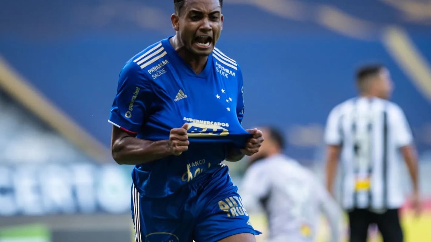 Jogador do Cruzeiro comemora gol em clássico contra o Atlético-MG, com adversário ao fundo