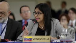 Delcy Rodríguez fala ao microfone em reunião internacional, com placa da Venezuela à frente
