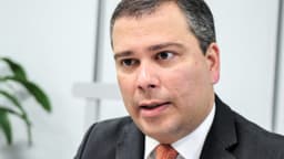 Paulo Henrique Costa, ex-presidente do BRB, fala em entrevista vestindo terno escuro e gravata laranja