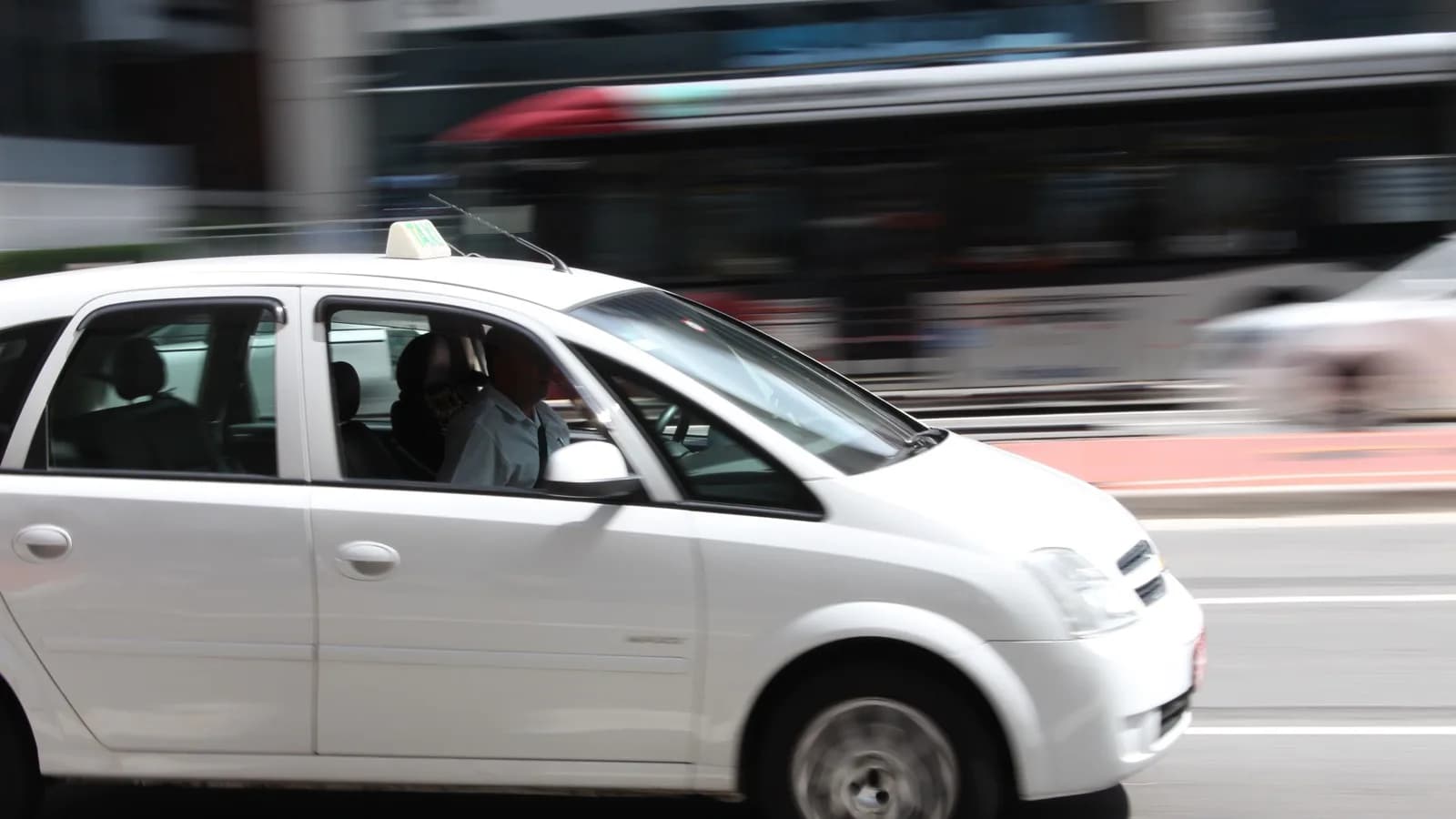 Táxi branco com motorista e passageira em movimento em avenida de São Paulo