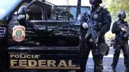 Agentes armados da Polícia Federal ao lado de viatura durante operação