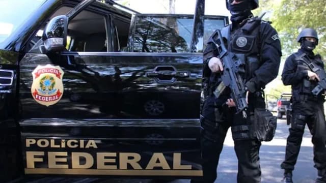 Agentes armados da Polícia Federal ao lado de viatura durante operação