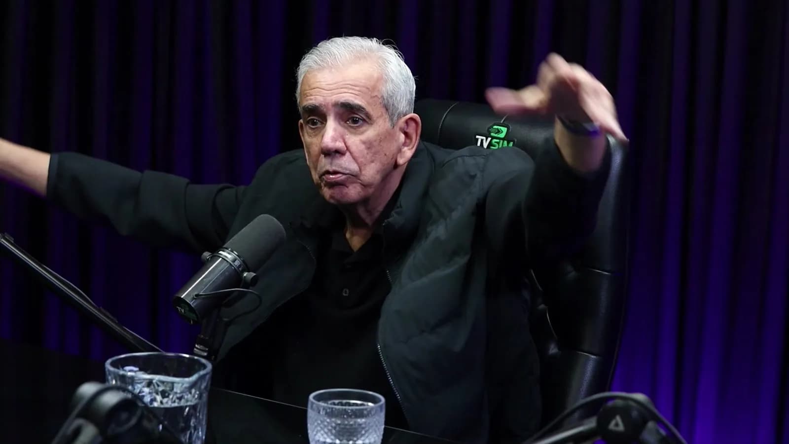 Ricardo Teagano gesticula com as duas mãos abertas durante entrevista em estúdio, ao narrar o momento do acidente