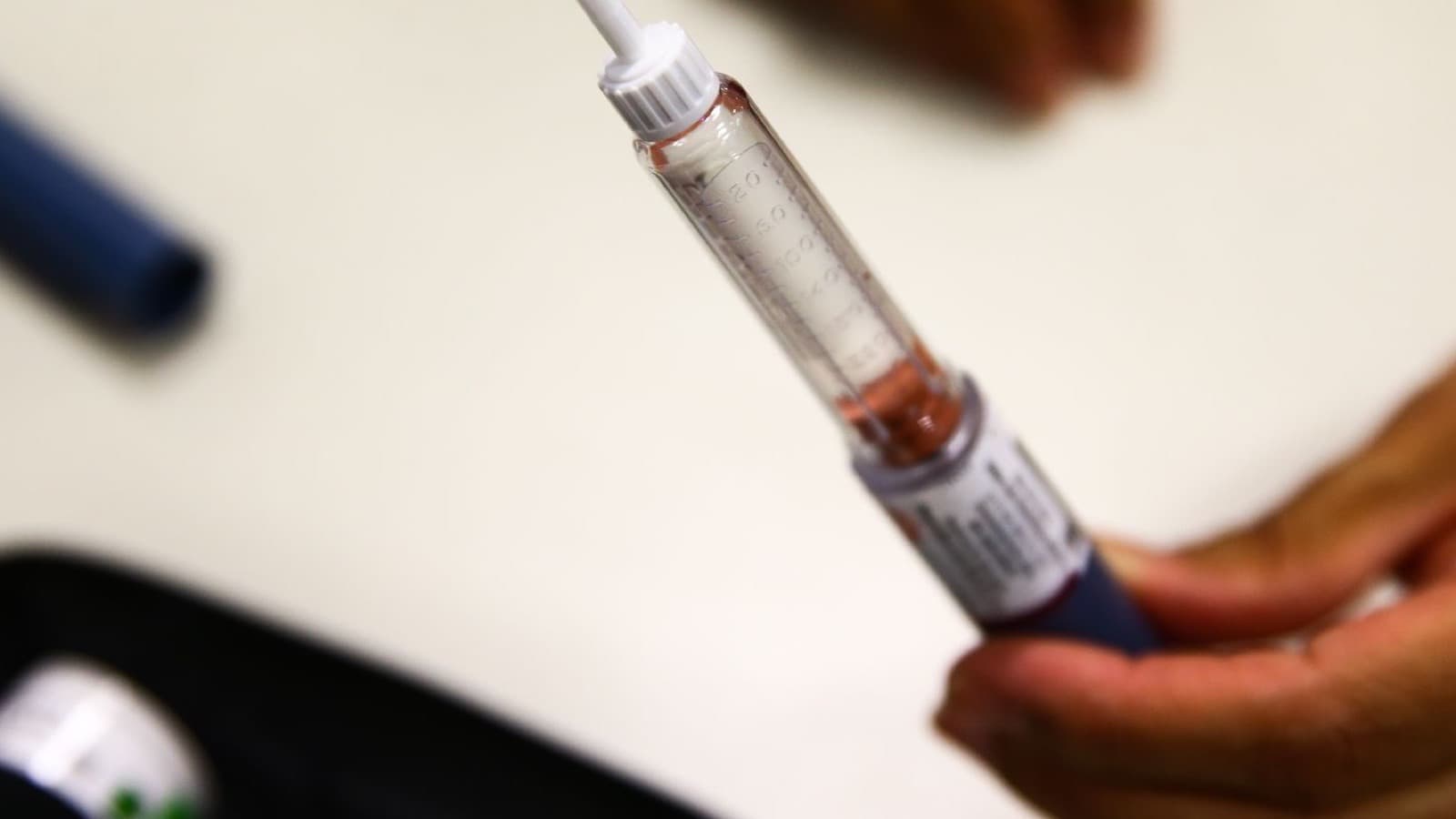 Close de uma mão segurando uma caneta de aplicação de insulina sobre uma mesa clara; imagem de contexto, não mostra os produtos de semaglutida recém-registrados