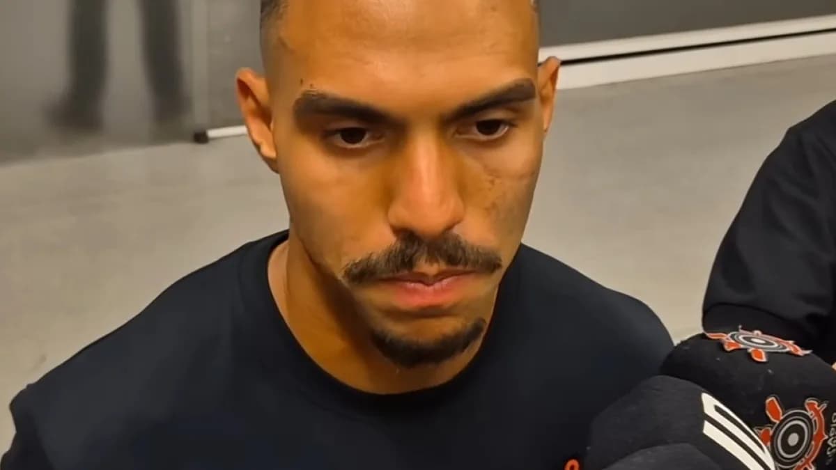 Matheuzinho concede entrevista a microfones de rádio e TV, com o cabelo loiro platinado e camisa preta do Corinthians