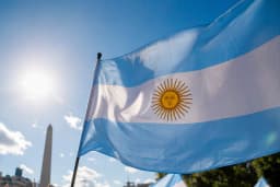 Bandeira da Argentina tremulando ao vento sob céu azul, com o Obelisco de Buenos Aires ao fundo, ilustrando o feriado nacional declarado após a campanha da seleção na Copa do Mundo