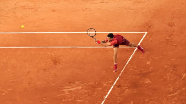 Novak Djokovic se estica para alcançar a bola durante partida de tênis em quadra de saibro
