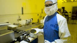 Pesquisadora com traje de sala limpa segura um wafer de silício em fábrica de semicondutores