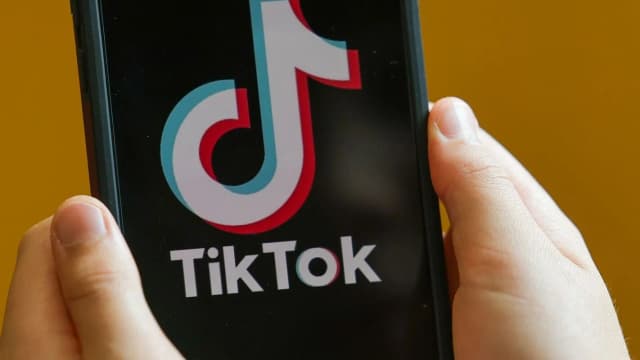 Mãos seguram um celular com o aplicativo TikTok aberto na tela