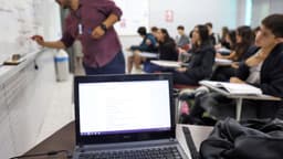 Sala de aula de curso superior com professor no quadro branco e estudantes com cadernos, foto de arquivo ilustrativa sobre financiamento estudantil