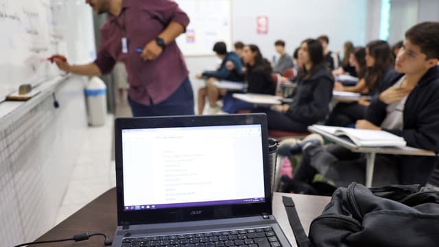 Sala de aula de curso superior com professor no quadro branco e estudantes com cadernos, foto de arquivo ilustrativa sobre financiamento estudantil