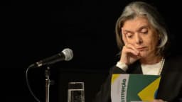Ministra Cármen Lúcia lê um exemplar da Constituição durante evento, com microfone à frente