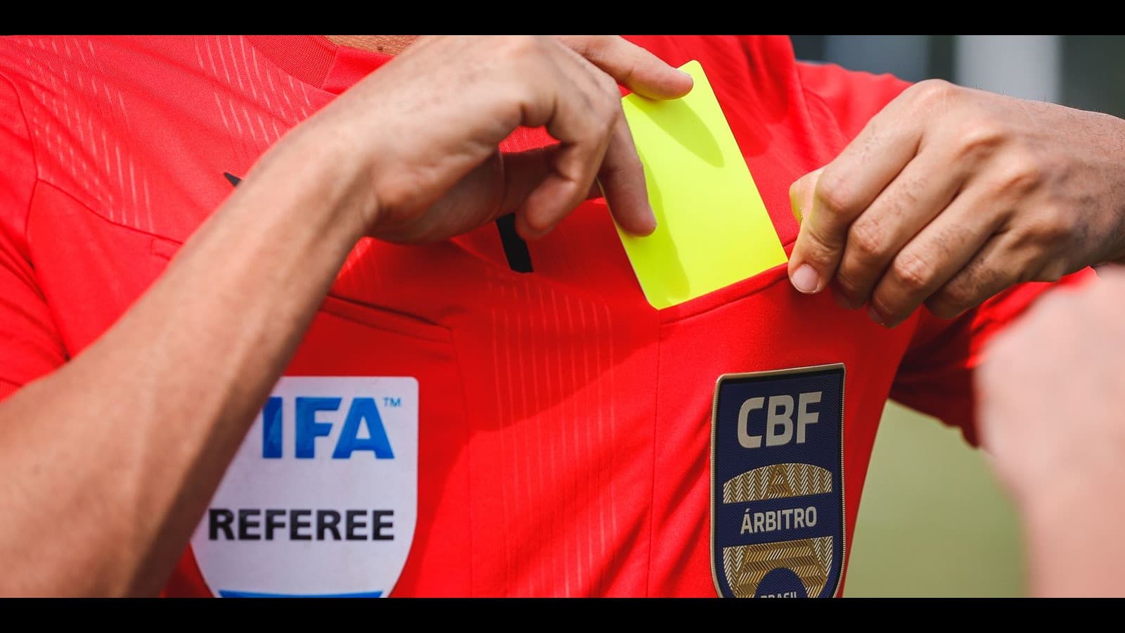 Árbitro de futebol brasileiro guarda cartão amarelo no bolso da camisa, com emblema da CBF (foto de arquivo, ilustrativa)