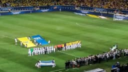 Bandeira gigante é carregada por torcedores em campo antes de partida de futebol