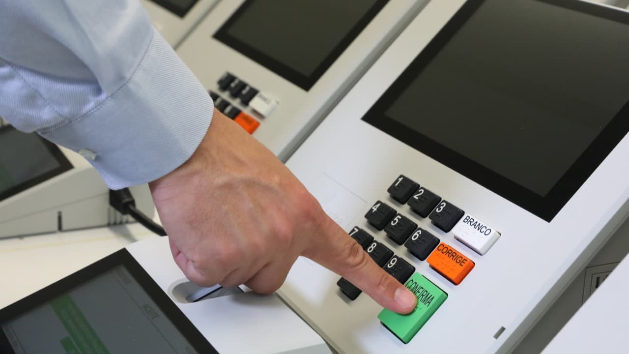 Mão de eleitor digitando número em urna eletrônica brasileira