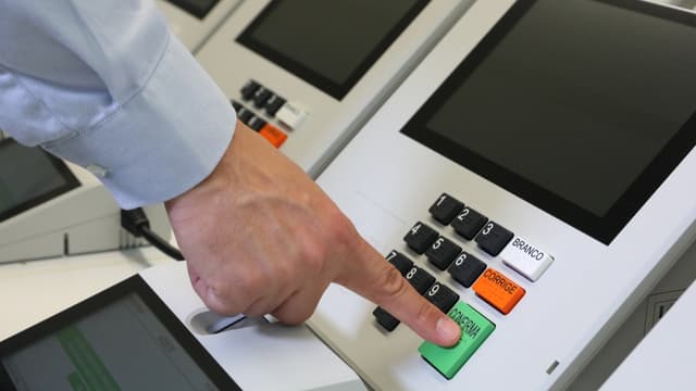 Mão de eleitor digitando número em urna eletrônica brasileira