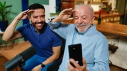 Lula e André Janones sorriem e fazem gesto de continência enquanto gravam vídeo com um celular