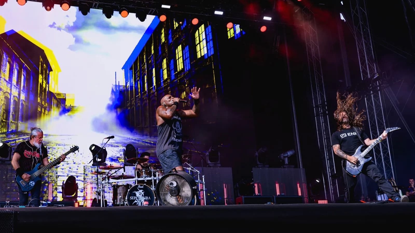 Sepultura se apresenta ao vivo no palco, com o baterista atrás do bumbo escrito Sepultura 40