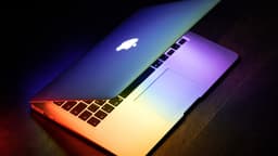 MacBook Air de 2015 semiaberto sobre mesa de madeira, iluminado por luzes coloridas
