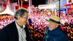 Lula cumprimenta apoiador em comício de campanha à noite, com multidão ao fundo