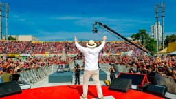 Lula de costas, de braços erguidos, diante de multidão em palco vermelho durante lançamento de campanha em 2026