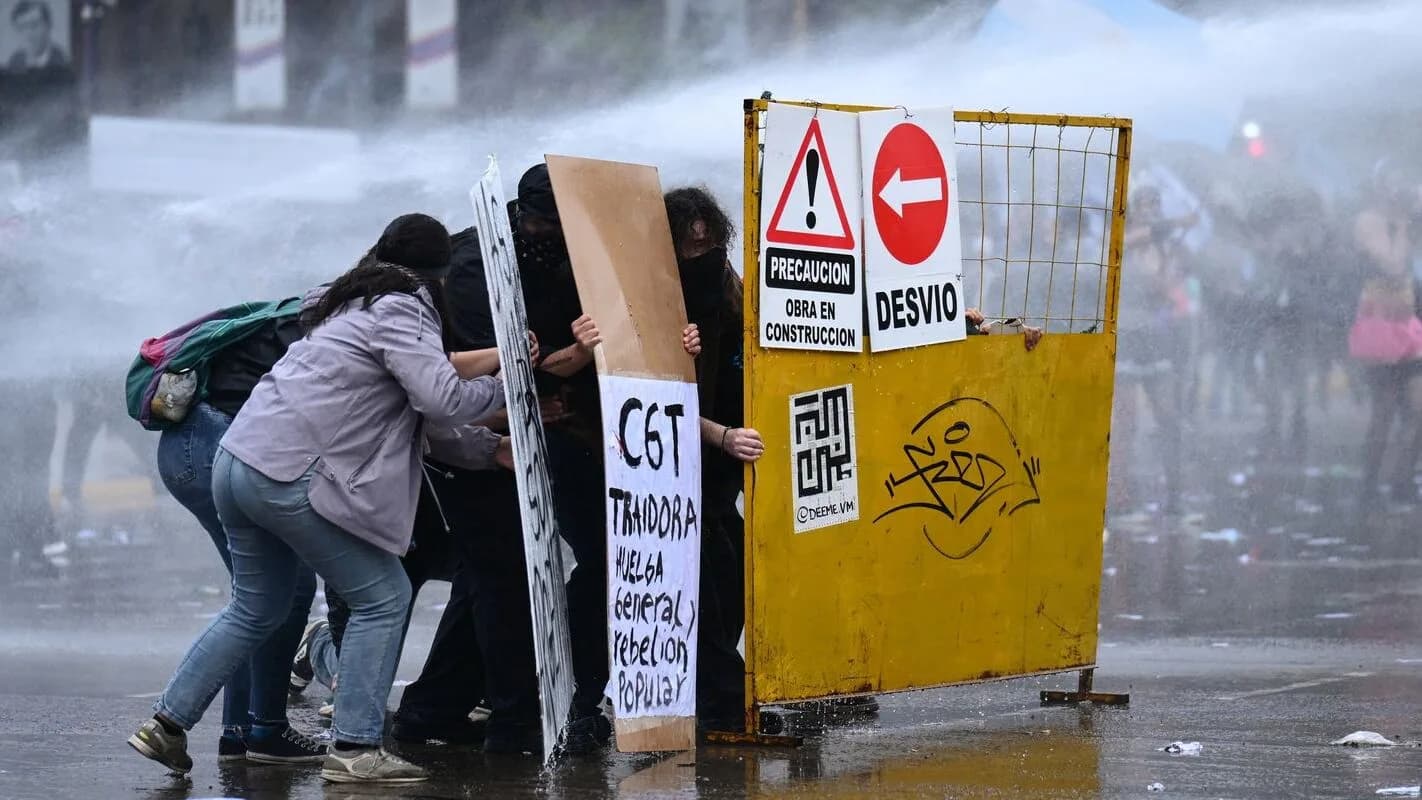 Manifestantes se protegem de jato de água durante protesto contra o governo de Javier Milei na Argentina