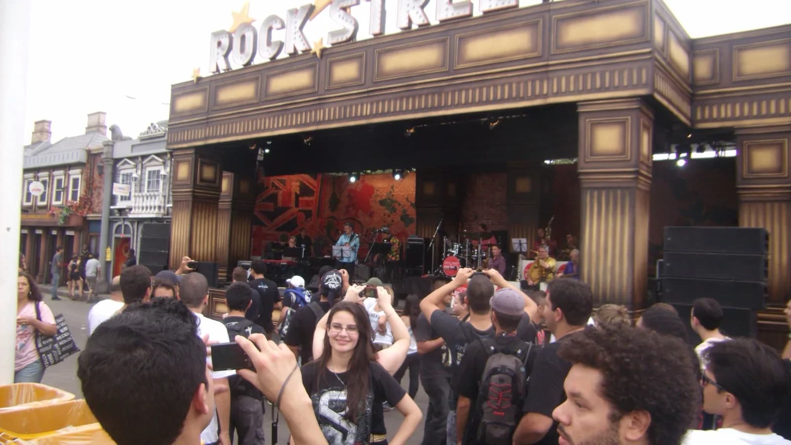 Multidão fotografa banda se apresentando no palco Rock Street, com estrutura decorada em estilo retrô